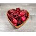 Handcrafted, heart-shaped wooden bowl filled with red apple cinnamon potpourri on a grey wood-grain surface